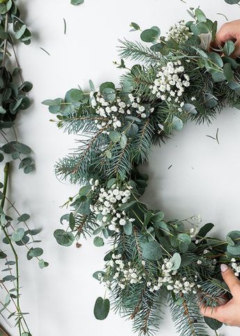 Ein selbstgemachter Adventskranz aus dunkelgrünen Tannenzweigen und weißen Blumen auf einem weißen Hintergrund